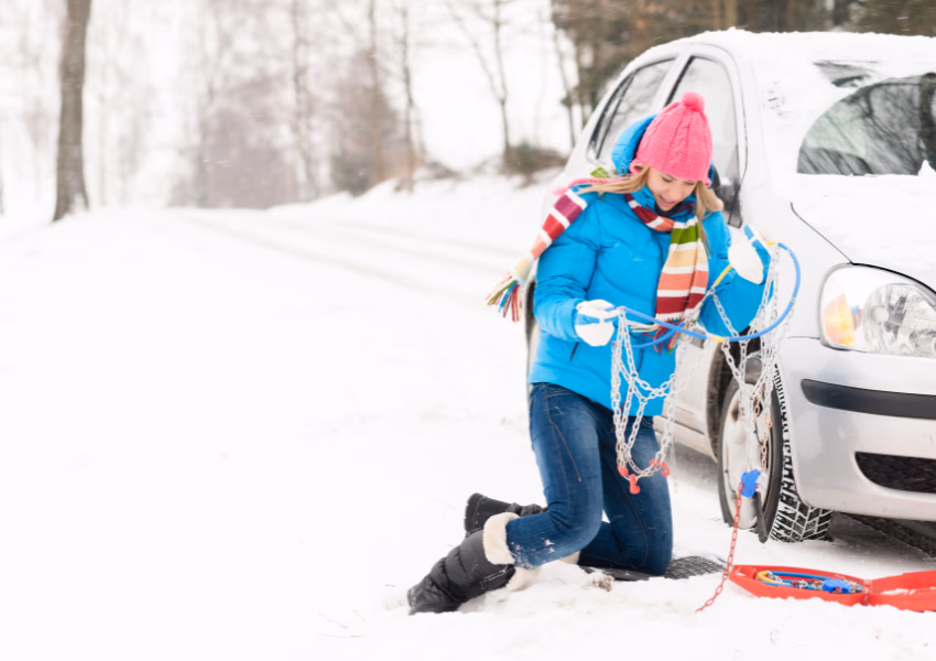 an image of a woman installing tire chains on a car stuck in snow