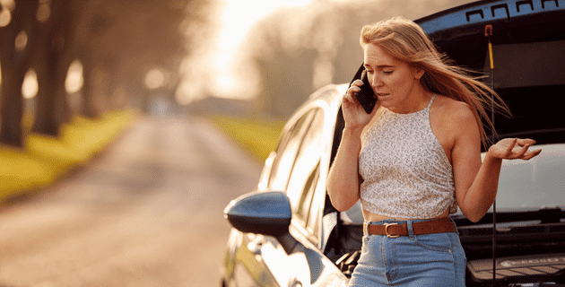 woman using cell phone standing by a broken-down car