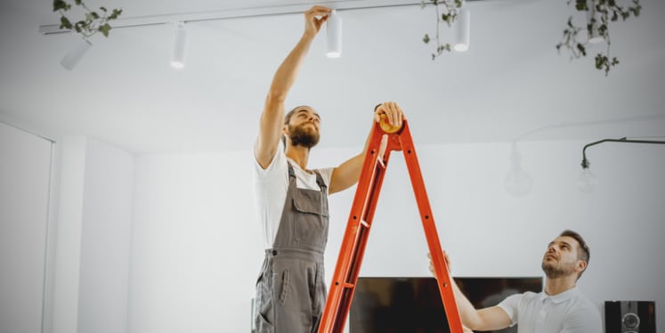 one person on ladder changing light while another person holds ladder